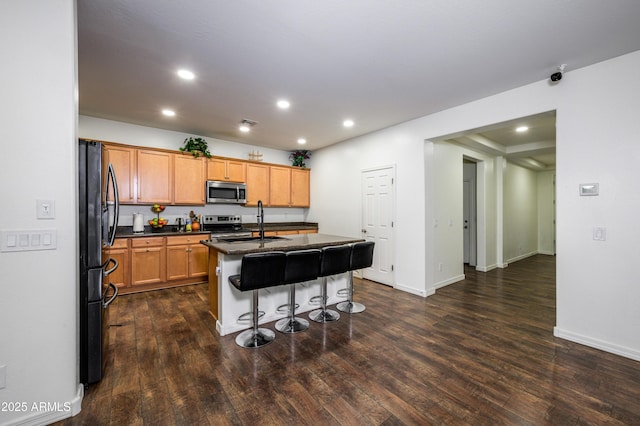 kitchen with a kitchen island with sink, a kitchen breakfast bar, sink, dark hardwood / wood-style floors, and appliances with stainless steel finishes