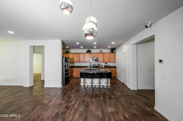 kitchen featuring dark hardwood / wood-style flooring, stainless steel appliances, a kitchen island with sink, sink, and a breakfast bar area