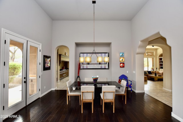 9842 E Celtic Dr, Scottsdale, AZ 85260 - dining area featuring arched walkways, hardwood / wood-style flooring, a towering ceiling, baseboards, and a chandelier