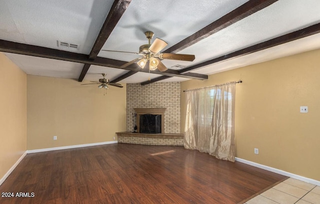 unfurnished living room featuring a brick fireplace, light hardwood / wood-style floors, ceiling fan, beam ceiling, and a textured ceiling