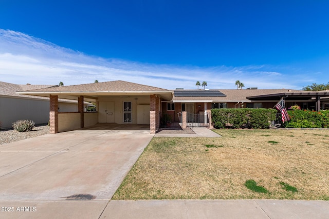 single story home featuring a carport, solar panels, concrete driveway, and a front yard