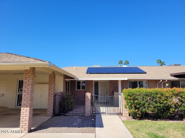 ranch-style home featuring solar panels, a gate, and a shingled roof