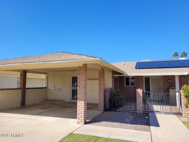 ranch-style house featuring driveway, fence, roof with shingles, an attached carport, and solar panels