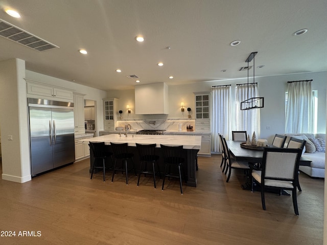 kitchen featuring hardwood / wood-style floors, a spacious island, built in refrigerator, a kitchen bar, and white cabinetry