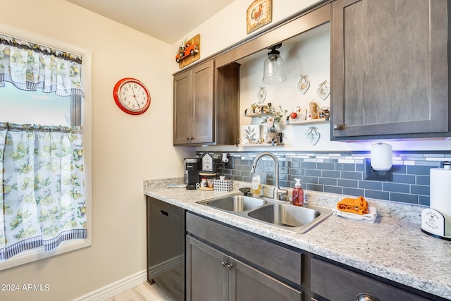 kitchen with decorative backsplash, dark brown cabinets, light stone counters, dishwasher, and sink