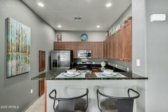 kitchen with appliances with stainless steel finishes, visible vents, a peninsula, and dark stone countertops