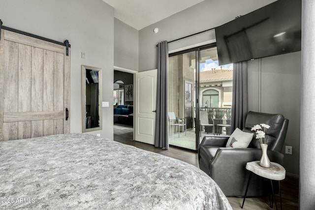 bedroom with access to outside, wood finished floors, a towering ceiling, and a barn door