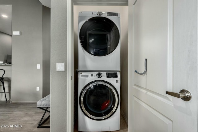 clothes washing area with laundry area, stacked washer / drying machine, and wood finished floors