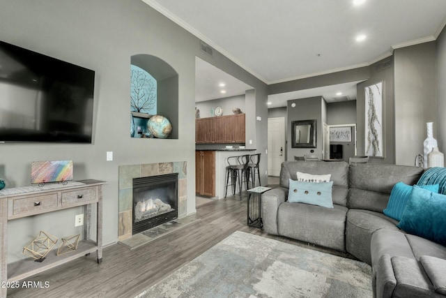 living room with recessed lighting, wood finished floors, visible vents, a tiled fireplace, and crown molding