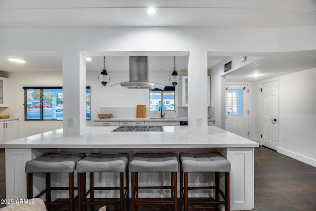 kitchen with light stone counters, island range hood, stainless steel gas cooktop, and a breakfast bar area