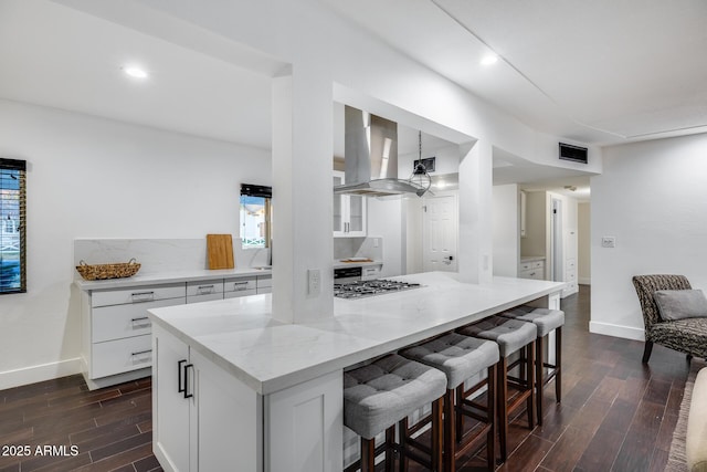 kitchen with a breakfast bar, white cabinetry, a center island, exhaust hood, and stainless steel gas stovetop