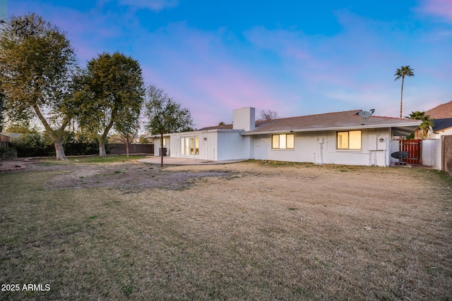 back house at dusk featuring a yard and a patio