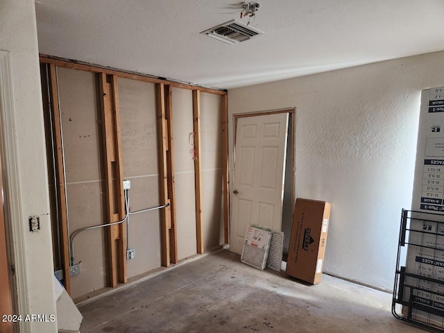 interior space featuring a textured wall, visible vents, and unfinished concrete flooring