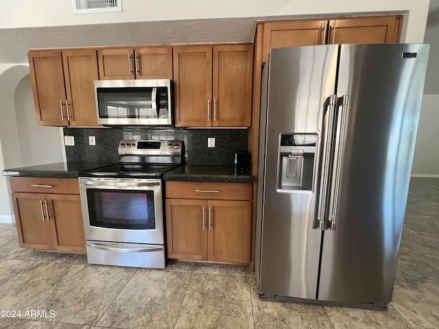 15230 N Blackbird Dr, Fountain Hills, AZ 85268 - kitchen featuring stainless steel appliances, brown cabinetry, decorative backsplash, arched walkways, and baseboards