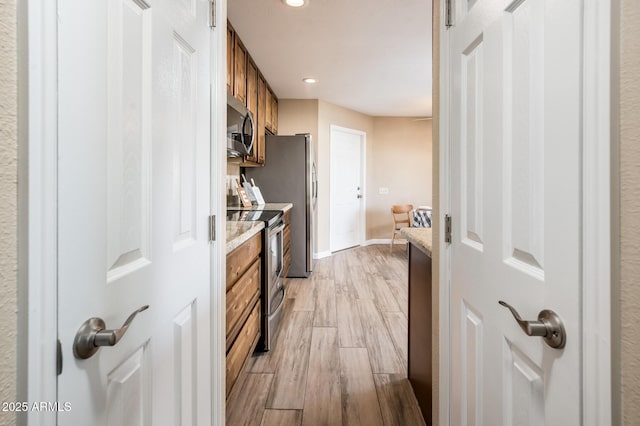 kitchen with stainless steel appliances, light stone countertops, and light wood-type flooring