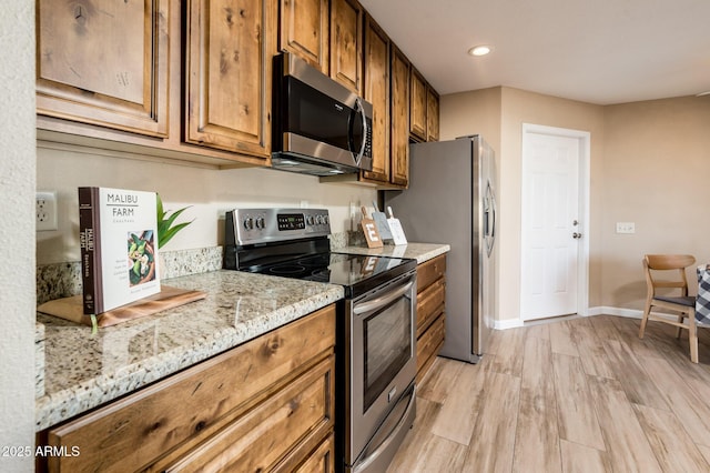 kitchen with stainless steel appliances, light stone countertops, and light hardwood / wood-style flooring