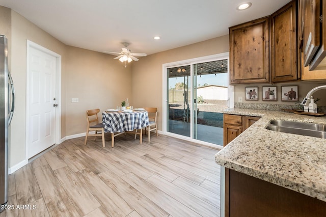 kitchen with sink, light stone counters, stainless steel fridge, ceiling fan, and light hardwood / wood-style floors