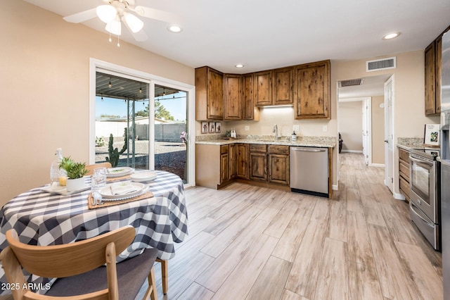 kitchen featuring appliances with stainless steel finishes, sink, ceiling fan, light stone counters, and light wood-type flooring