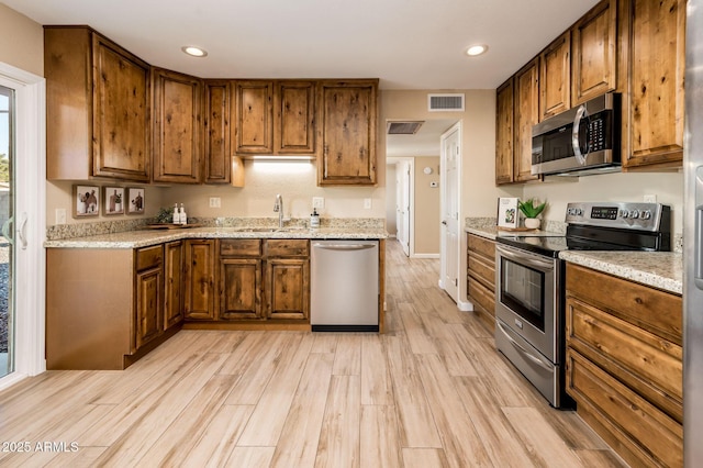 kitchen with sink, light hardwood / wood-style flooring, light stone countertops, and appliances with stainless steel finishes