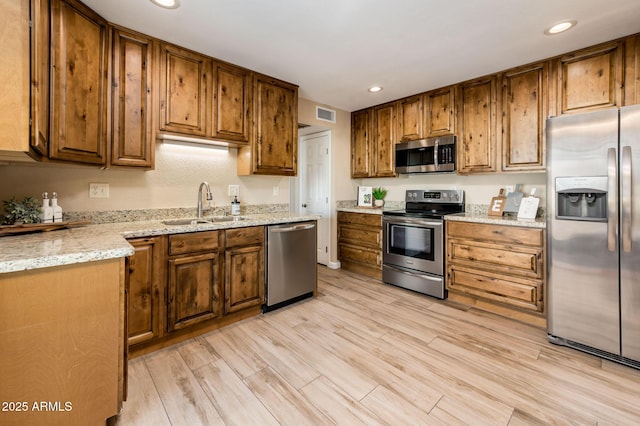 kitchen with appliances with stainless steel finishes, light hardwood / wood-style floors, sink, and light stone countertops