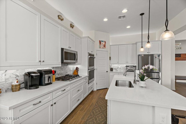 kitchen with pendant lighting, stainless steel appliances, tasteful backsplash, and a center island with sink