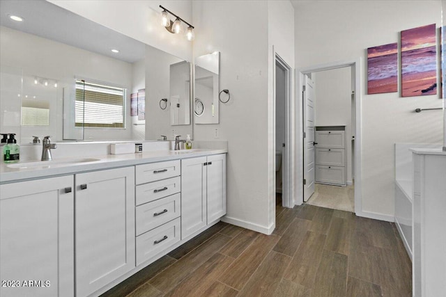 bathroom with a bathtub, oversized vanity, dual sinks, and hardwood / wood-style flooring