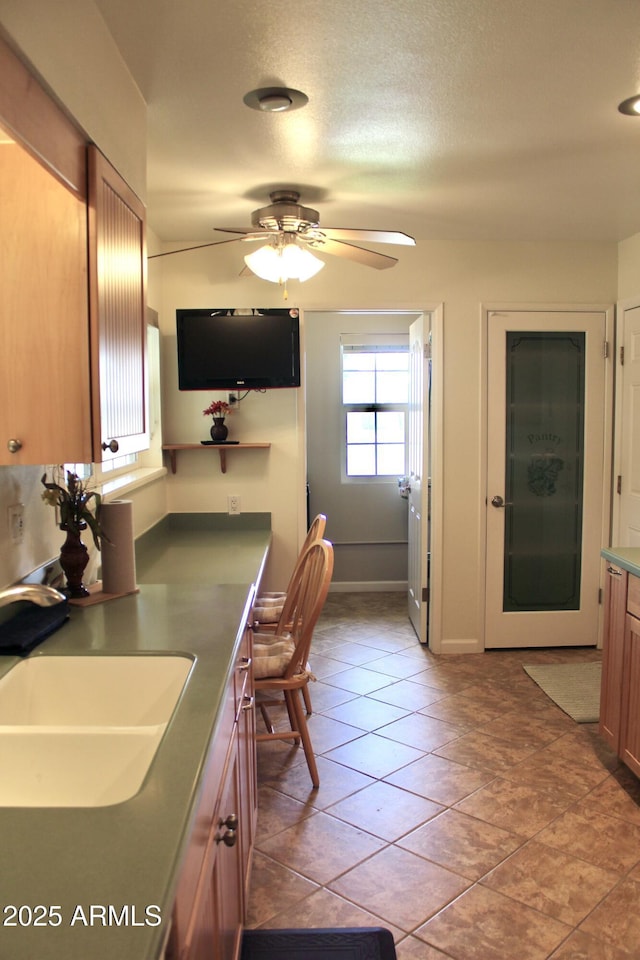 kitchen featuring a textured ceiling, light tile patterned floors, a sink, a ceiling fan, and baseboards