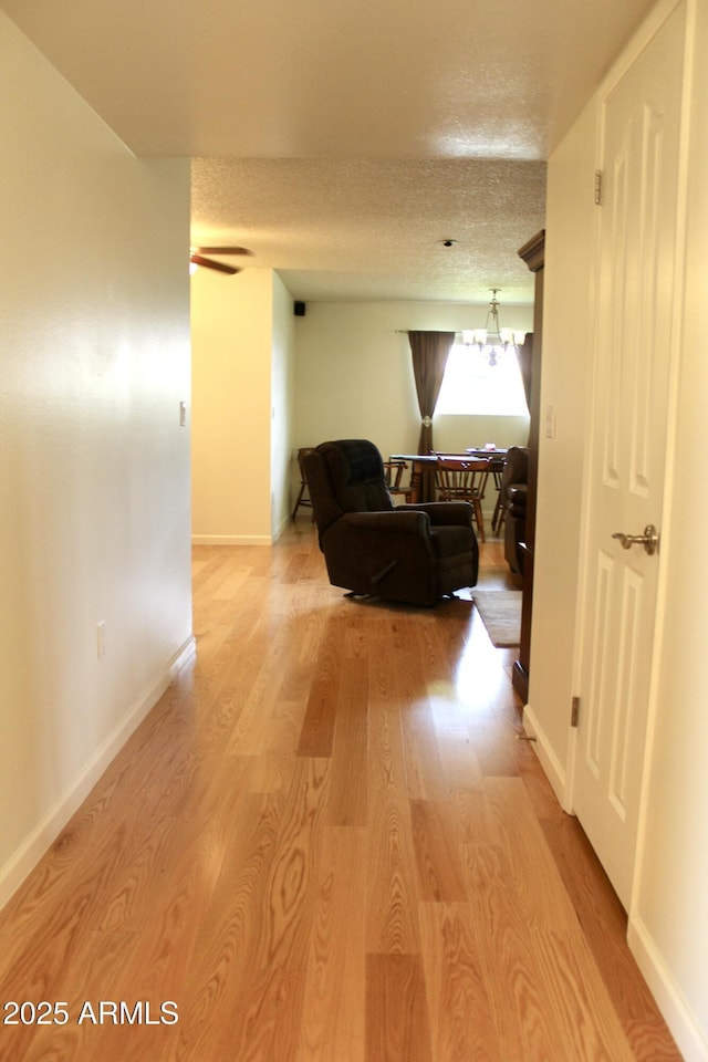 corridor featuring a textured ceiling, baseboards, and light wood-style floors