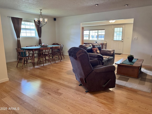 living area featuring light wood-type flooring, a notable chandelier, a textured ceiling, and baseboards