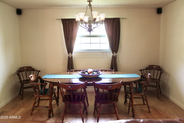 dining space featuring baseboards, a textured ceiling, wood finished floors, and a notable chandelier