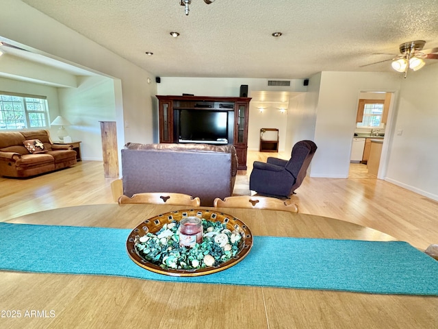 living area with visible vents, ceiling fan, a textured ceiling, and wood finished floors