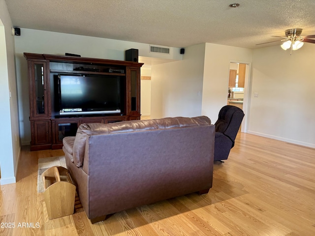 living area with ceiling fan, a textured ceiling, light wood-style flooring, visible vents, and baseboards