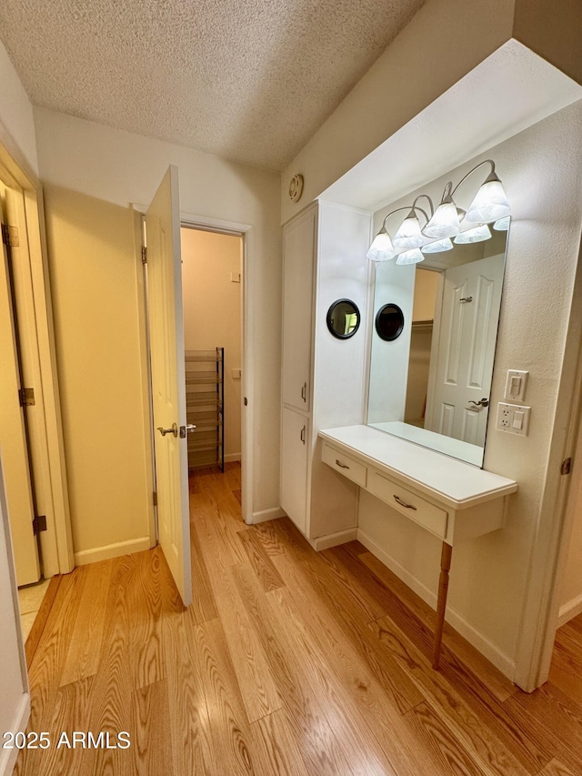 mudroom with baseboards, a textured ceiling, and light wood finished floors