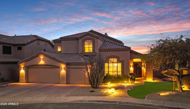 mediterranean / spanish-style home featuring an attached garage, a tile roof, concrete driveway, and stucco siding