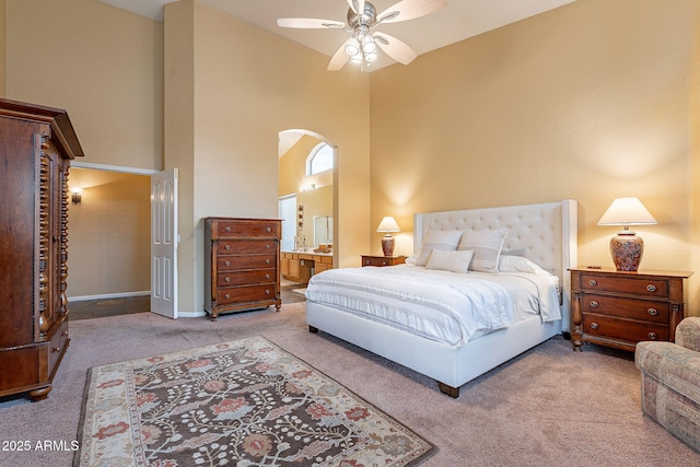 bedroom with a ceiling fan, connected bathroom, arched walkways, carpet, and a towering ceiling