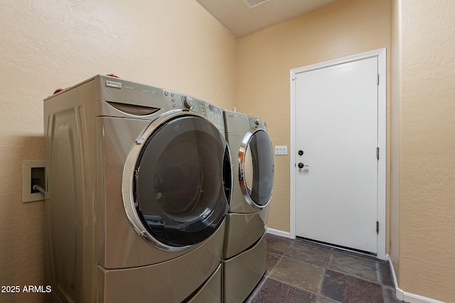 washroom with baseboards, laundry area, a textured wall, stone tile flooring, and independent washer and dryer