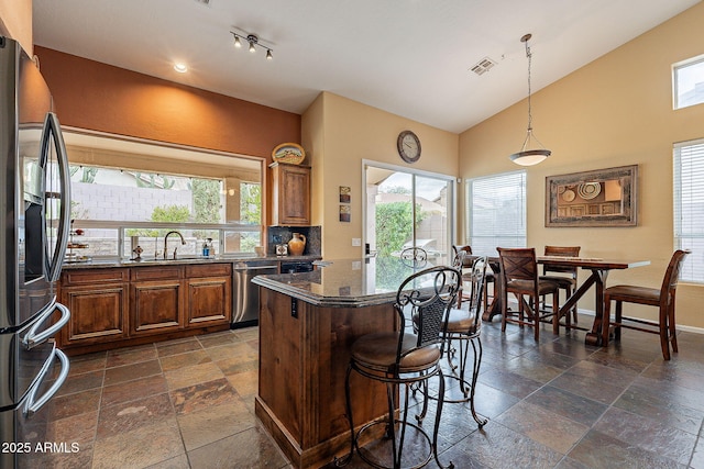 kitchen featuring a sink, a kitchen island, stone tile floors, appliances with stainless steel finishes, and a breakfast bar area