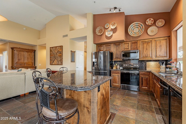 kitchen with open floor plan, a kitchen bar, appliances with stainless steel finishes, brown cabinetry, and a sink