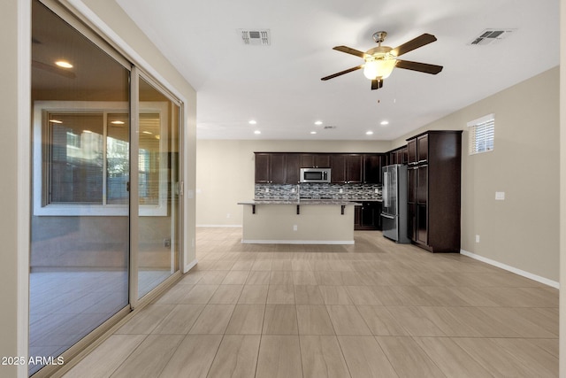 kitchen featuring visible vents, decorative backsplash, appliances with stainless steel finishes, dark brown cabinets, and a kitchen breakfast bar