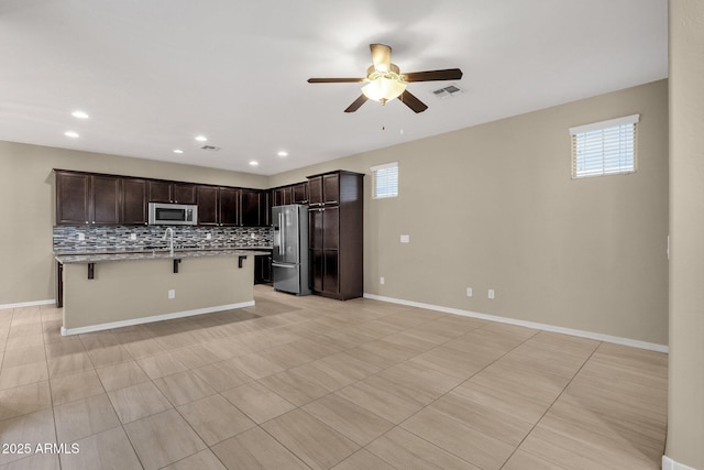 kitchen with dark brown cabinetry, visible vents, a kitchen breakfast bar, stainless steel appliances, and backsplash