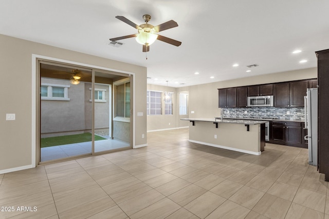 kitchen featuring a breakfast bar area, visible vents, dark brown cabinets, backsplash, and stainless steel microwave