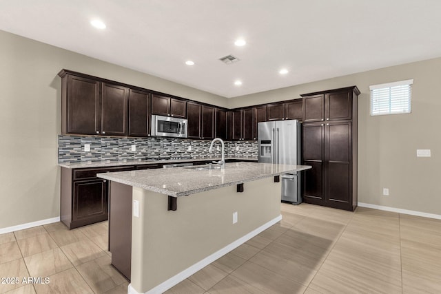 kitchen with light stone countertops, visible vents, a kitchen breakfast bar, appliances with stainless steel finishes, and decorative backsplash