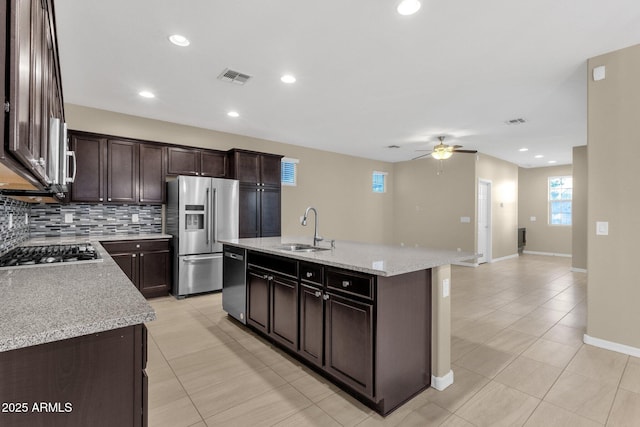 kitchen with a sink, dark brown cabinets, appliances with stainless steel finishes, backsplash, and a center island with sink