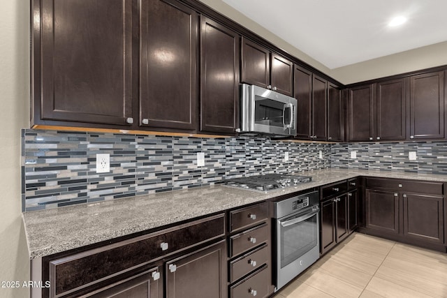 kitchen with light stone countertops, dark brown cabinetry, appliances with stainless steel finishes, and backsplash