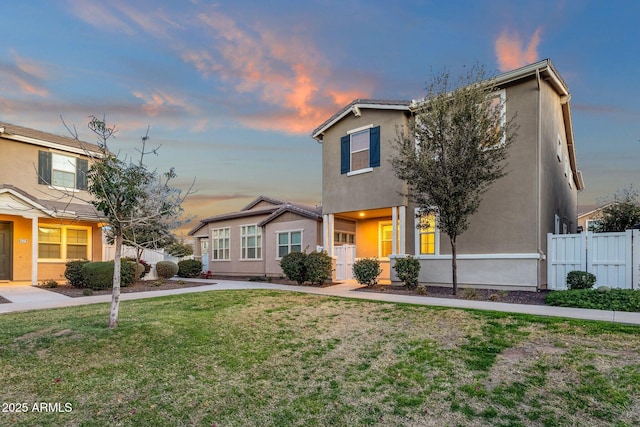 view of front of house featuring fence, a front lawn, and stucco siding