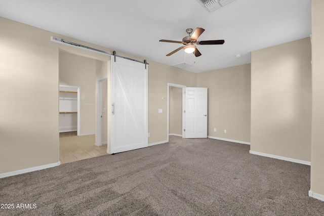 unfurnished bedroom with a barn door, carpet flooring, visible vents, and baseboards