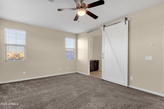 unfurnished bedroom featuring ceiling fan, a barn door, connected bathroom, baseboards, and carpet