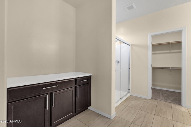 bathroom with a spacious closet, a shower stall, visible vents, and baseboards