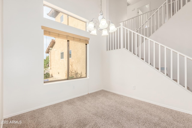 unfurnished room with carpet, a high ceiling, and an inviting chandelier