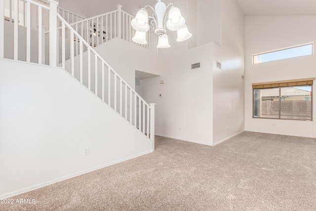 unfurnished living room featuring carpet floors, a high ceiling, and a notable chandelier